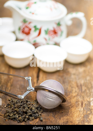 trockenen grünen chinesischen Tee-Set, mit Sieb Closeup, Tassen und Teekanne auf Hintergrund über alte Holzplatte Stockfoto