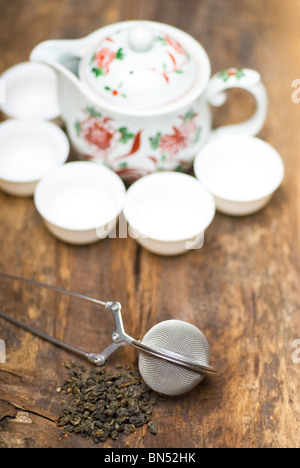 trockenen grünen chinesischen Tee-Set, mit Sieb Closeup, Tassen und Teekanne auf Hintergrund über alte Holzplatte Stockfoto