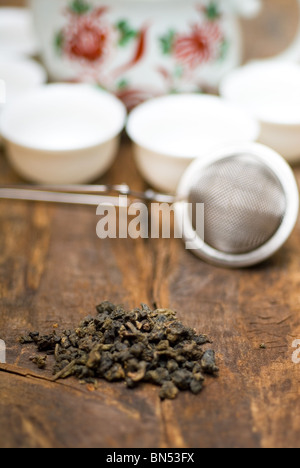 trockenen grünen chinesischen Tee-Set, mit Sieb Closeup, Tassen und Teekanne auf Hintergrund über alte Holzplatte Stockfoto