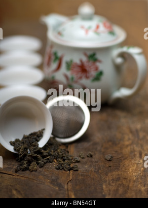 trockenen grünen chinesischen Tee-Set, mit Sieb Closeup, Tassen und Teekanne auf Hintergrund über alte Holzplatte Stockfoto
