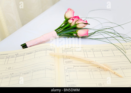 Eine Hochzeit Register und Feder mit einem Bouquet von rosa Rosen auf einem weißen Tisch. Stockfoto