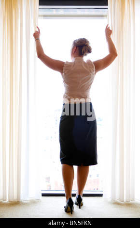 Frau in der Hotelsuite, ziehen Sie die Vorhänge zurück. Stockfoto