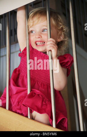 Mädchen Kleinkind saß auf der Treppe zu Hause lachen durch das Geländer Geländer Modell veröffentlicht Stockfoto