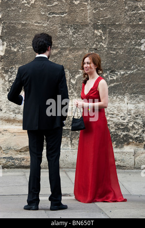 Eine rothaarige Frau in einem roten Kleid spricht, ein hochgewachsener Mann im Frack außerhalb der Wadham College-Ball im Juni in Oxford. Stockfoto