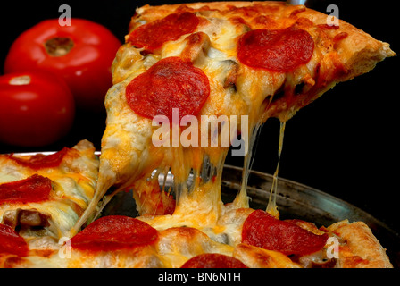 Stück Salami Pizza ganze Pizza mit Tomaten im Hintergrund entfernt. Auf schwarzem Hintergrund isoliert. Stockfoto