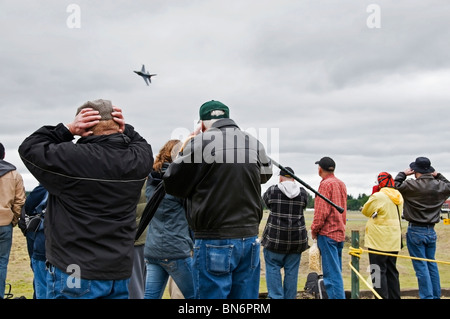 Eine Gruppe von Menschen ihre Ohren bedecken und beobachten Sie die schnelle Annäherung und Antenne Stunt von einer f-16 Fighting Falcon auf einer Airshow. Stockfoto