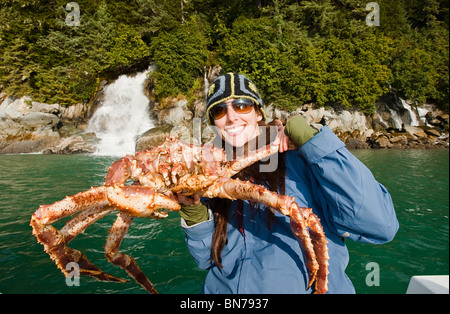 Frau hält eine Sportart gefangen Königskrabbe in Berners Bucht mit Berners fällt im Hintergrund, Alaska Stockfoto