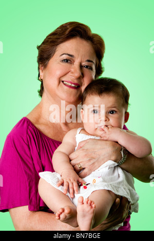 Schöne glücklich senior kaukasischen Hispanic Latina Großmutter Holding niedlichen Baby in Armen, auf einem grünen Hintergrund. Stockfoto