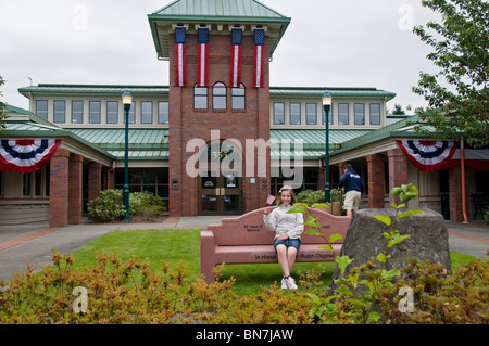 Ein kleines Mädchen mit einer Fahne sitzt auf einer Bank vor dem Rathaus Tumwater am Independence Day, während sie für die Parade wartet. Stockfoto