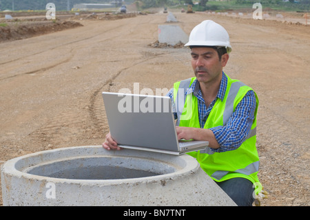 Hispanische Bauarbeiter mit Laptop in Feld Stockfoto