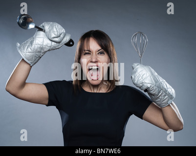 Frau Stamm hält Küchenstudio Utensilien isoliert auf grauem Hintergrund Stockfoto