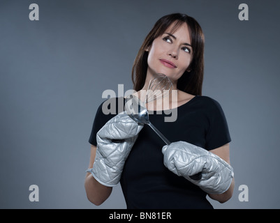 eine Kaukasische Frau denken Holding isoliert Küchenstudio Utensilien auf grauem Hintergrund Stockfoto