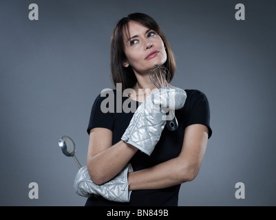 eine Frau denken Holding isoliert Küchenstudio Utensilien auf grauem Hintergrund Stockfoto