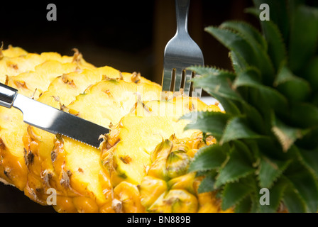 lebendige reifer Ananas in Scheiben geschnitten auf einem schwarzen Teller mit Messer und Gabel Stockfoto