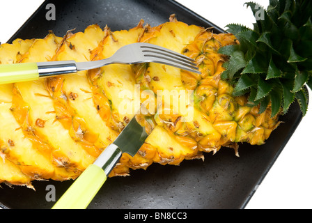 lebendige reifer Ananas in Scheiben geschnitten auf einem schwarzen Teller mit Messer und Gabel Stockfoto