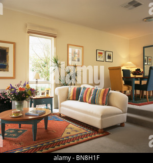 Bunt gestreifte Kissen auf weißen Sofa und bunt gemusterten Teppich am Boden in moderner Split-Level-Wohnzimmer und Esszimmer Stockfoto