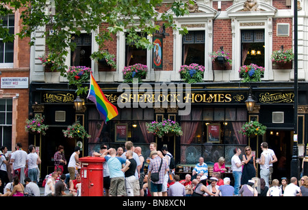 Eine Gay Pride Flagge und ein Publikum außerhalb der Sherlock Holmes Pub in London. Stockfoto