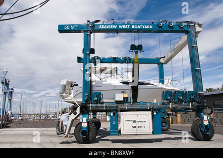 Ein Bayliner Motorboot ist in die Schlinge von einem Travelift gewiegt, nach wird aus dem Wasser durch die Seaview West-Werft geschleppt. Stockfoto