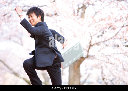 Unternehmer gehen mit Aktenkoffer unter Kirschblüten Stockfoto