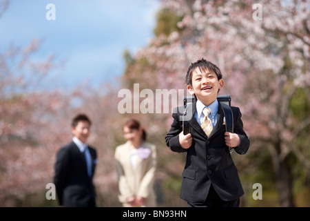 Volksschule Junge mit Eltern unter Kirschblüten Stockfoto