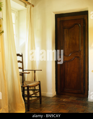 Antike Ladder-back Stuhl vor cremefarbene Vorhänge im kleinen Saal mit Holztür Stockfoto