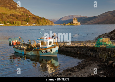 Fischer in Fischerboot & Eilean Donan Castle, Loch Duich, Schottisches Hochland, Schottland Stockfoto