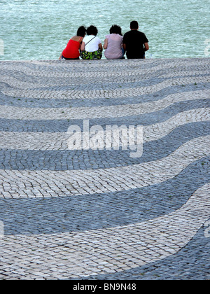 Ein Quartett von Menschen sitzen am Wasser mit Blick auf den Tejo in Lissabon Portugal Stockfoto