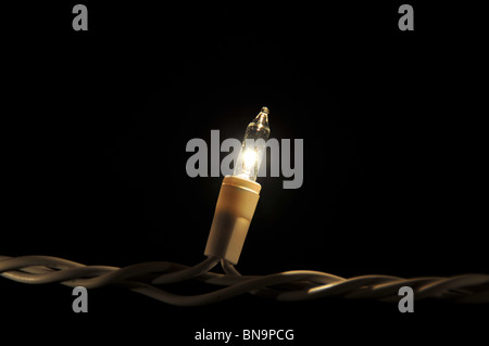 Singuläre Weihnachtslicht auf eine weiße Schnur auf einem schwarzen Hintergrund im Dunkeln. Stockfoto