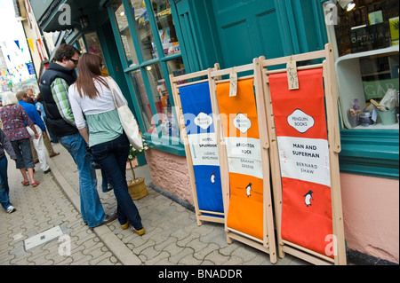 Literarische Liegestühle Marke Penguin Books zum Verkauf vor Geschäft mit Touristen zu Fuß vorbei und stöbern in Hay on Wye Wales UK Stockfoto