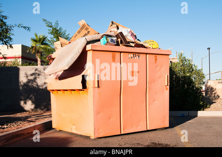 Eine Orange Müllcontainer ist voll von verschiedenen Arten von Müll und entleert werden kann. Stockfoto