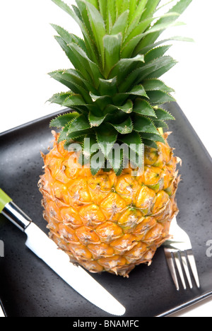 Reife lebendige Ananas auf einem schwarzen Teller mit Messer und Gabel Stockfoto