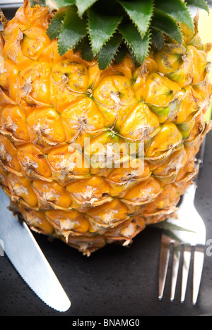 Reife lebendige Ananas auf einem schwarzen Teller mit Messer und Gabel Stockfoto