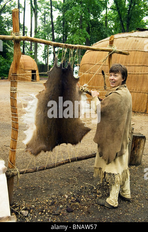 Dolmetscher, gekleidet wie ein Powhatan-Indianer schabt eine Tierhaut um Besucher in das frühe 1600 s in Jamestown Regelung, Virginia, USA Leben zeigen. Stockfoto