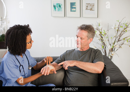 Krankenschwester besucht Mann mit Verletzung am Handgelenk Stockfoto