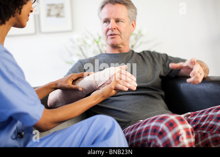 Krankenschwester besucht Mann mit Verletzung am Handgelenk Stockfoto