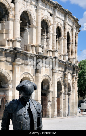 Die Bronzeskulptur eines Stierkämpfers steht in feierlicher Pose vor den riesigen, zweistöckigen Steinbögen der Arena von Nîmes, einem bemerkenswert gut geschützten Gebiet Stockfoto