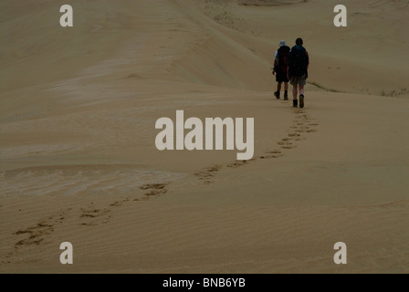 Zwei Wanderer Wandern auf dem Kamm einer Düne mit Rucksäcken. Footprints cross Rahmen und Ridge in die Ferne geht. Eastern Cape, Südafrika Stockfoto