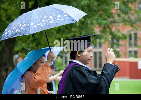 Eine glückliche graduate Unterstände unter einem Regenschirm nach seinem Abschluss Zeremonie an Universität von Birmingham nach Abschluss Ceremnoy. Stockfoto