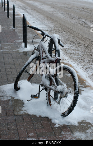 Eine verschneite Fahrrad ist angekettet an einen Posten in der Nähe der Straße in West Lafayette, Indiana Stockfoto