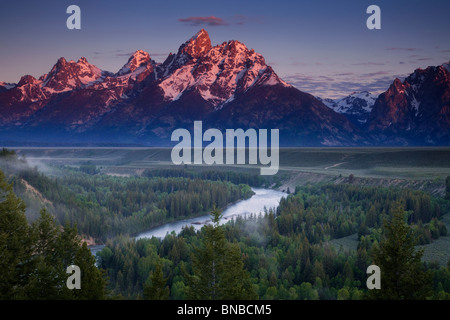 Sonnenlicht trifft die Gipfel des Grand Teton Berge im Morgengrauen aus der Snake River Overlook Stockfoto