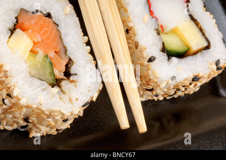 Makro von zwei Sushi Rollen über eine schwarze Platte mit Stäbchen. Flachen DOF Stockfoto