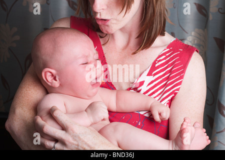 Mutter hält und versucht, ihre jungen Weinen und verärgert zu beruhigen Stockfoto