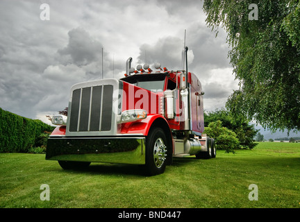 Ein roter Traktor Sattelschlepper auf einem grünen Rasen mit dramatische Wolken im Hintergrund. Stockfoto