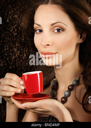 Schöne junge Frau hält eine rote Tasse Espresso Kaffee mit Kaffee Bohnen Hintergrund hinter ihr Stockfoto