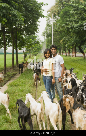 Paar stehend mit einer Herde von Ziegen in einem Feld, Kolkata, Westbengalen, Indien Stockfoto