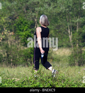 Eine Frau Kleid in schwarz Training Kleidung Powerwalking mit einer Flasche Wasser. Stockfoto