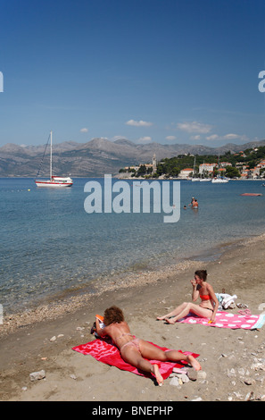 Frauen, Sonnenbaden am Strand und Blick auf Hafen Lopud Süd Dalmatien Kroatien dalmatinische kroatischen Insel Elafiti Elaphiten Inseln Stockfoto