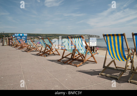 Linie der Liegestühle auf der konkreten Promenade oberhalb des Strandes in Swanage Bay, Dorset, UK. Stockfoto