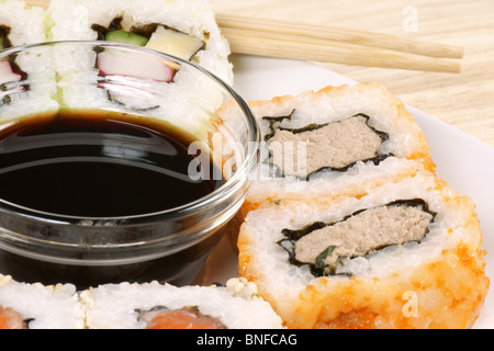 Nahaufnahme von Maki Sushi-Rollen serviert auf einem Teller mit Sojasauce und Stäbchen auf einem Holztisch Stockfoto