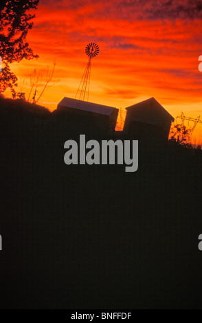 bewölktem Himmel leuchtend rote Sonnenuntergang Windmühle Bauernhof Gebäude Scheunen Stromleitungen kopieren Raum Stockfoto